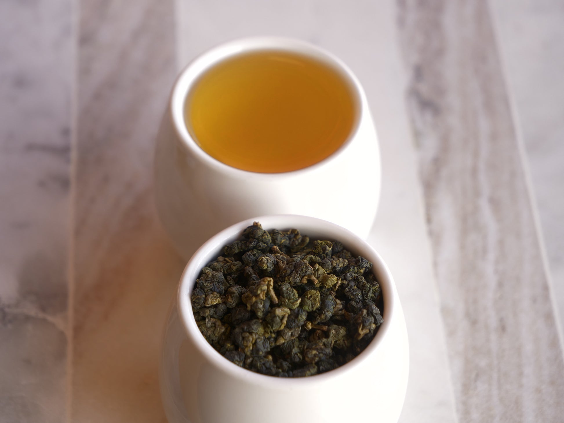 Two white containers with tea leaves and brewed tea on a marble surface