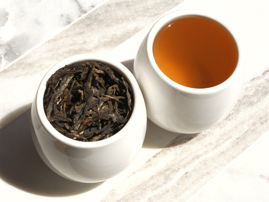 White ceramic bowl with tea leaves and a cup of brewed tea on a marble surface.