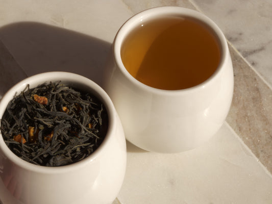 White cup of green tea next to a bowl of tea leaves on a marble surface.