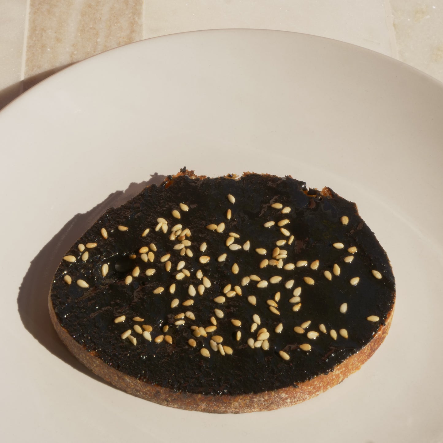 Round bread slice with black sesame spread and white sesame seeds on a white plate