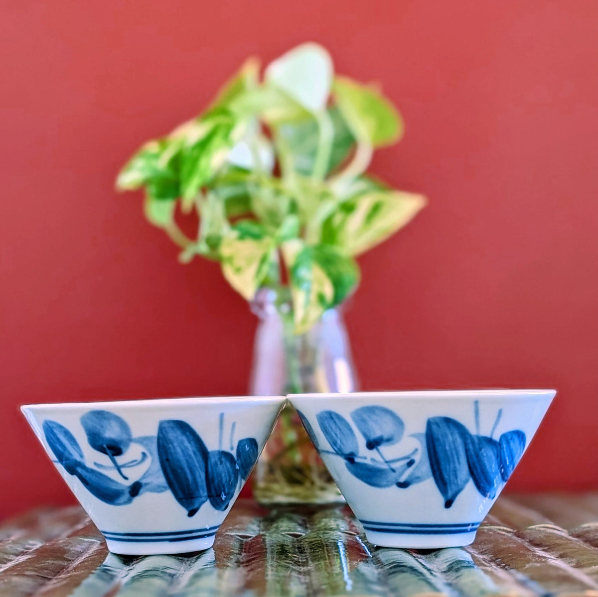 2 white porcelain tea cups painted with blue leaf design on a green mat against a terracotta background.