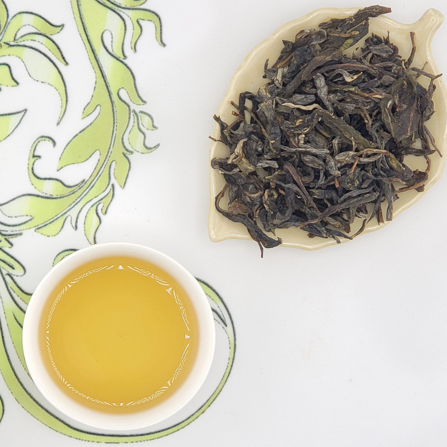 Specialty loose leaf Chinese tea next to a cup of golden hued tea.