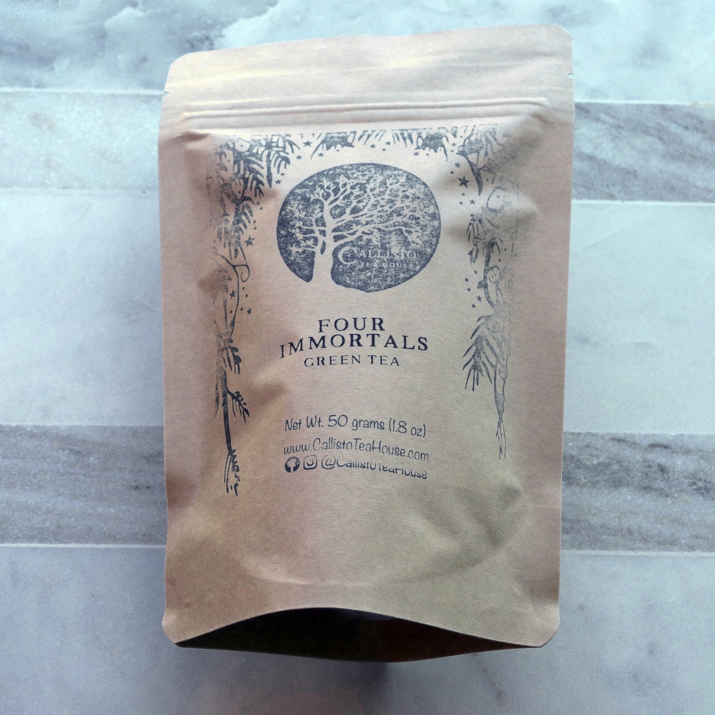 Kraft paper tea bag with 'Four Immortals Green Tea' branding on a marble surface.