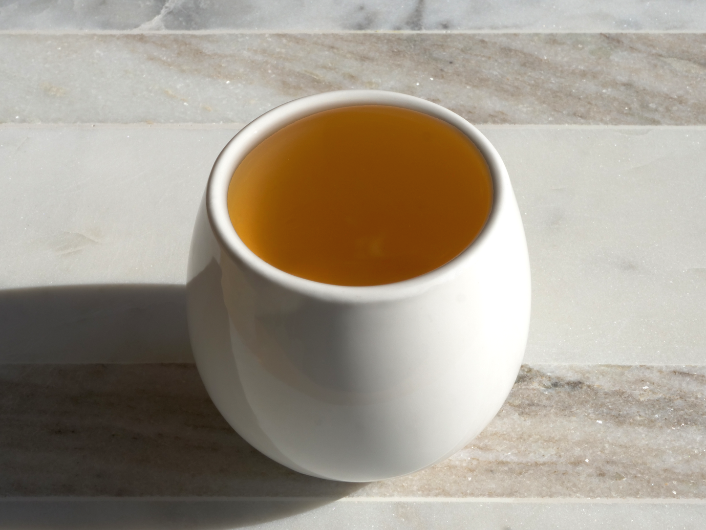 White ceramic cup filled with brewed green tea on a marble surface