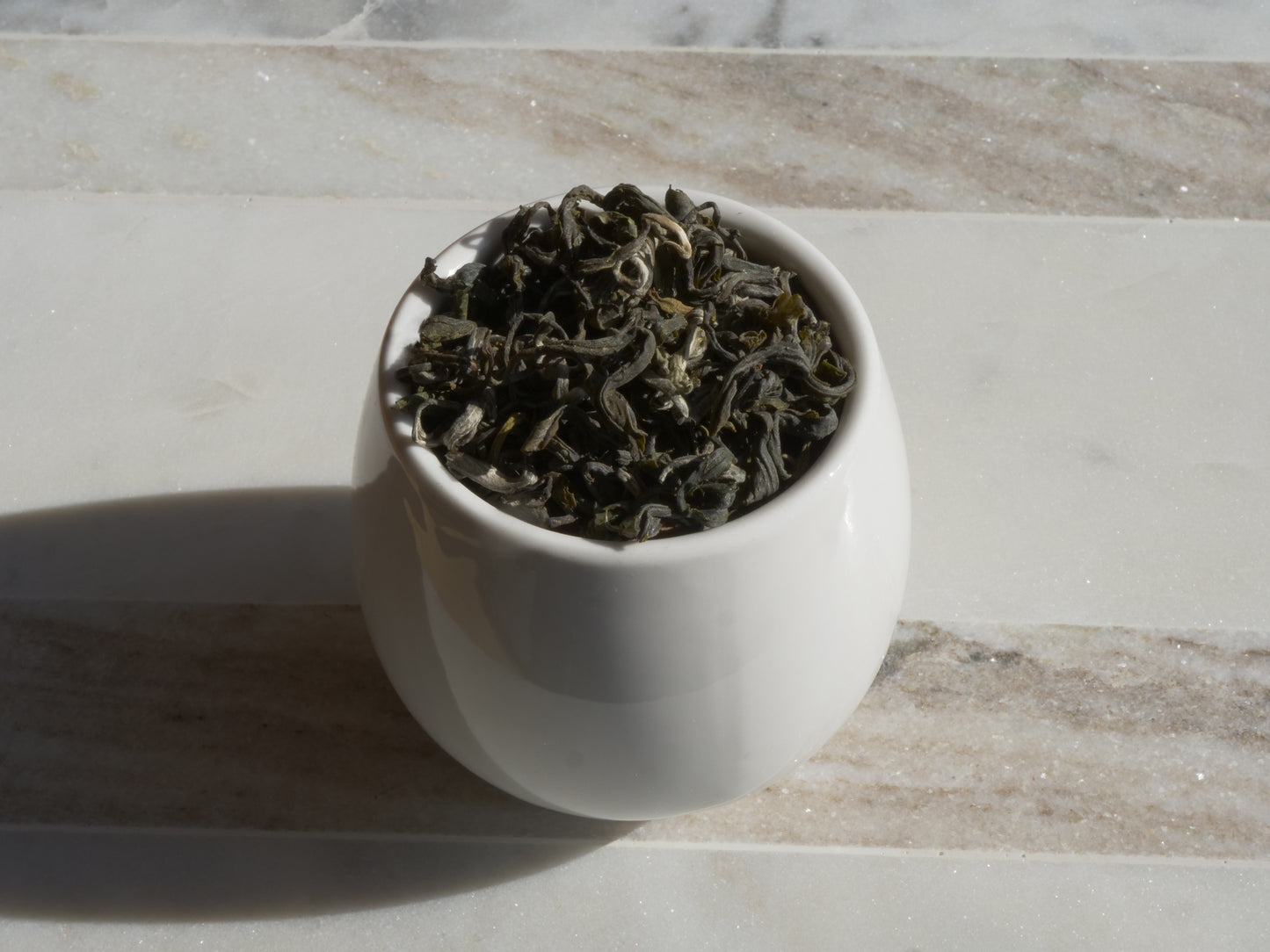 White ceramic bowl filled with green tea leaves on a marble surface