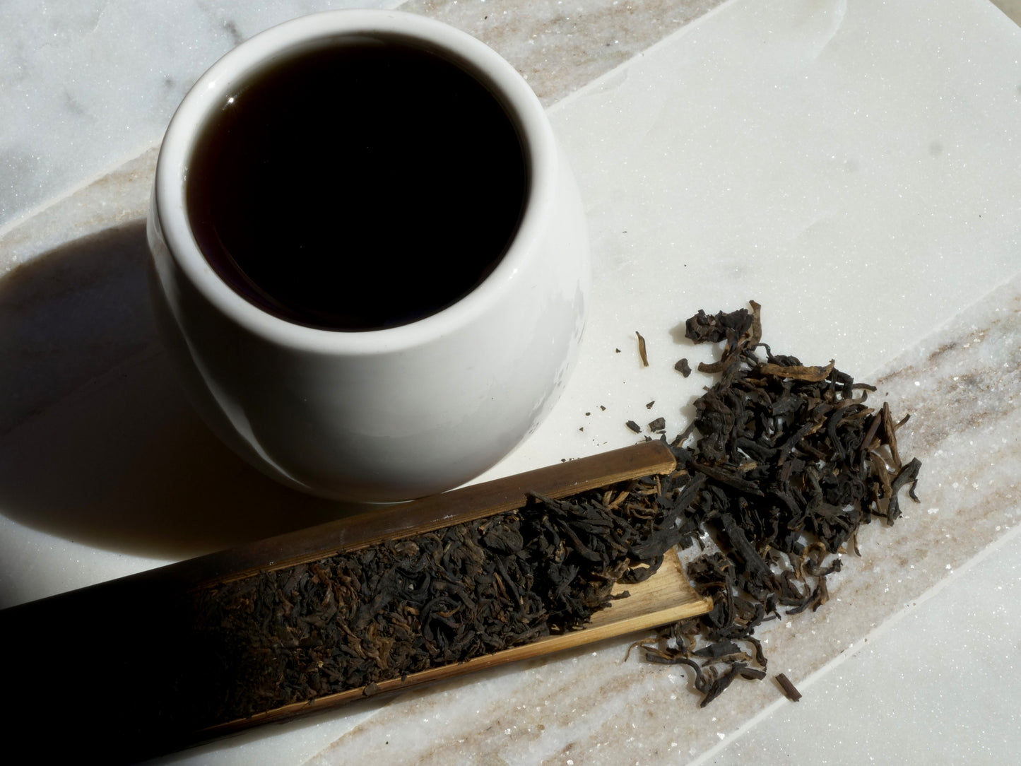White cup of dark tea with tea leaves on a marble surface