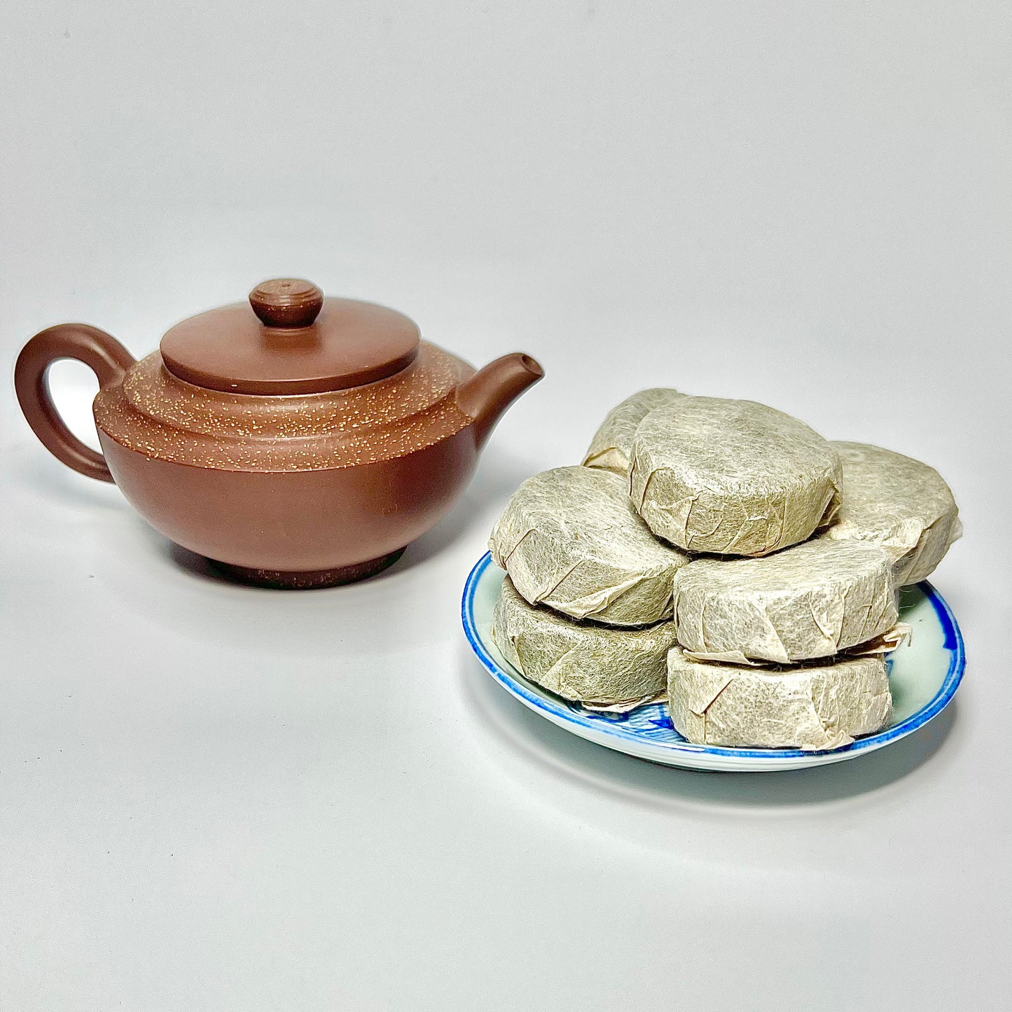 Pu-erh tea coins wrapped in paper next to a clay tea pot.