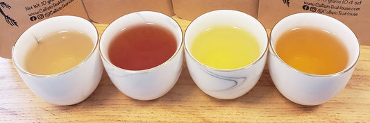 Four small teacups filled with teas ranging in color from bright yellow, light orange, amber, to burgundy.