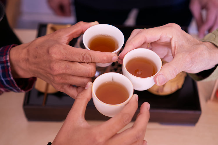 Three people holding white cups filled with tea in a close-up shot.