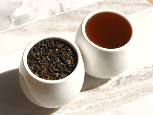 White ceramic container with dried tea leaves and a cup of brewed tea on a marble surface.