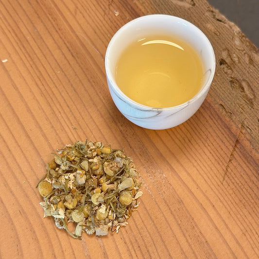 White cup of tea with dried chamomile flowers on a wooden surface