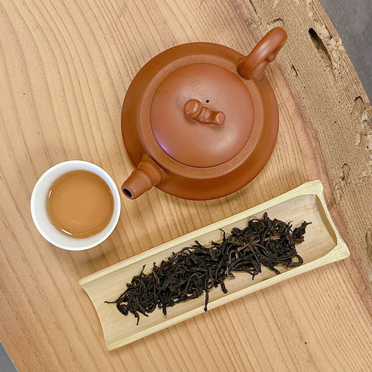 Clay teapot, white cup with tea, and wooden tray with tea leaves on a wooden surface