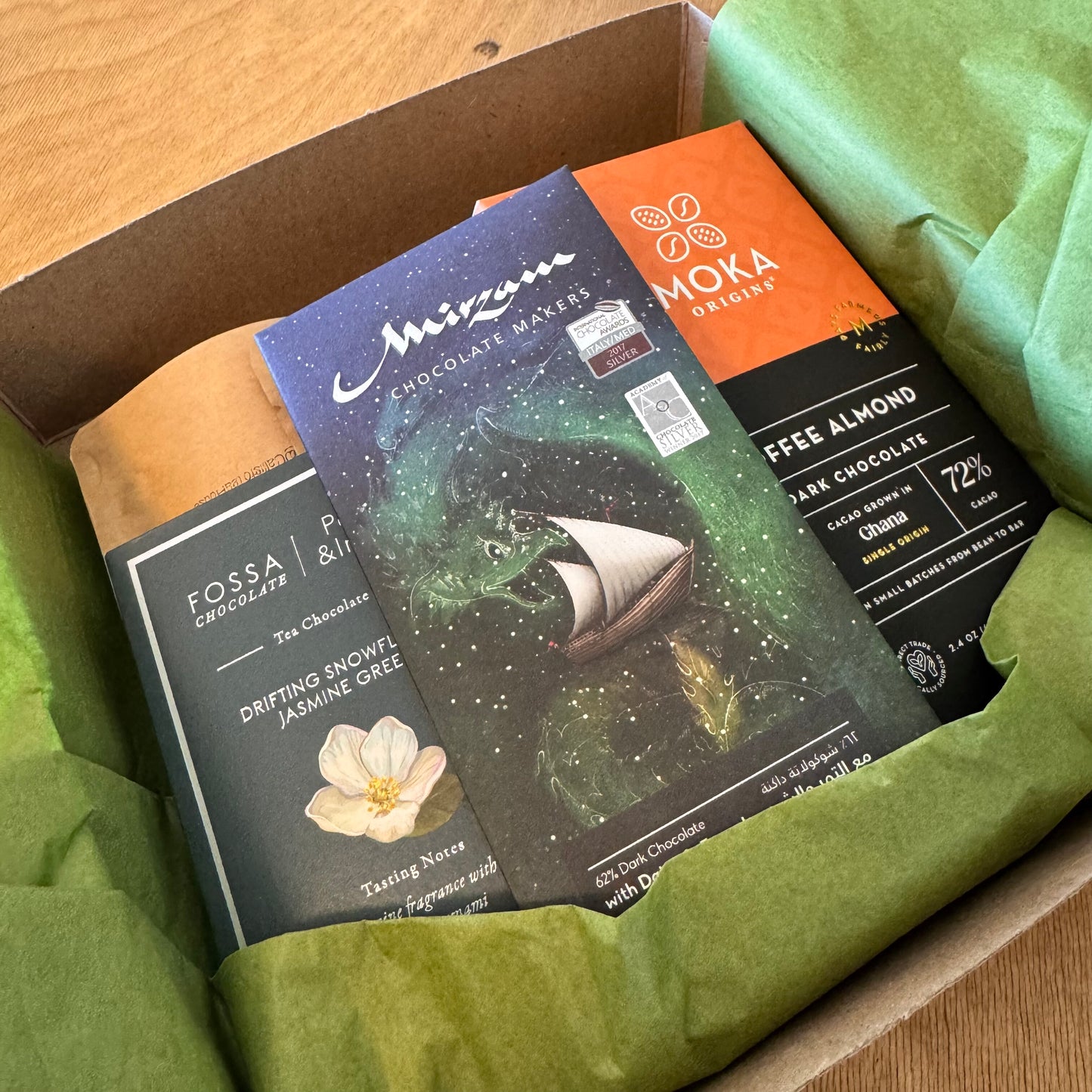 Assorted chocolate bars from different brands in a box with green tissue paper.