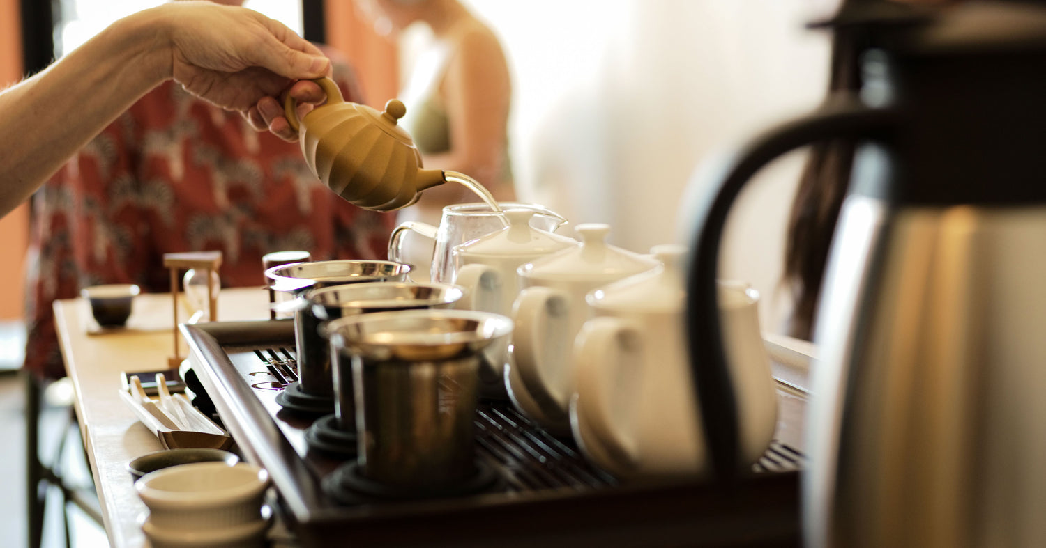 Person pouring tea from a teapot into cups on a tea tray.