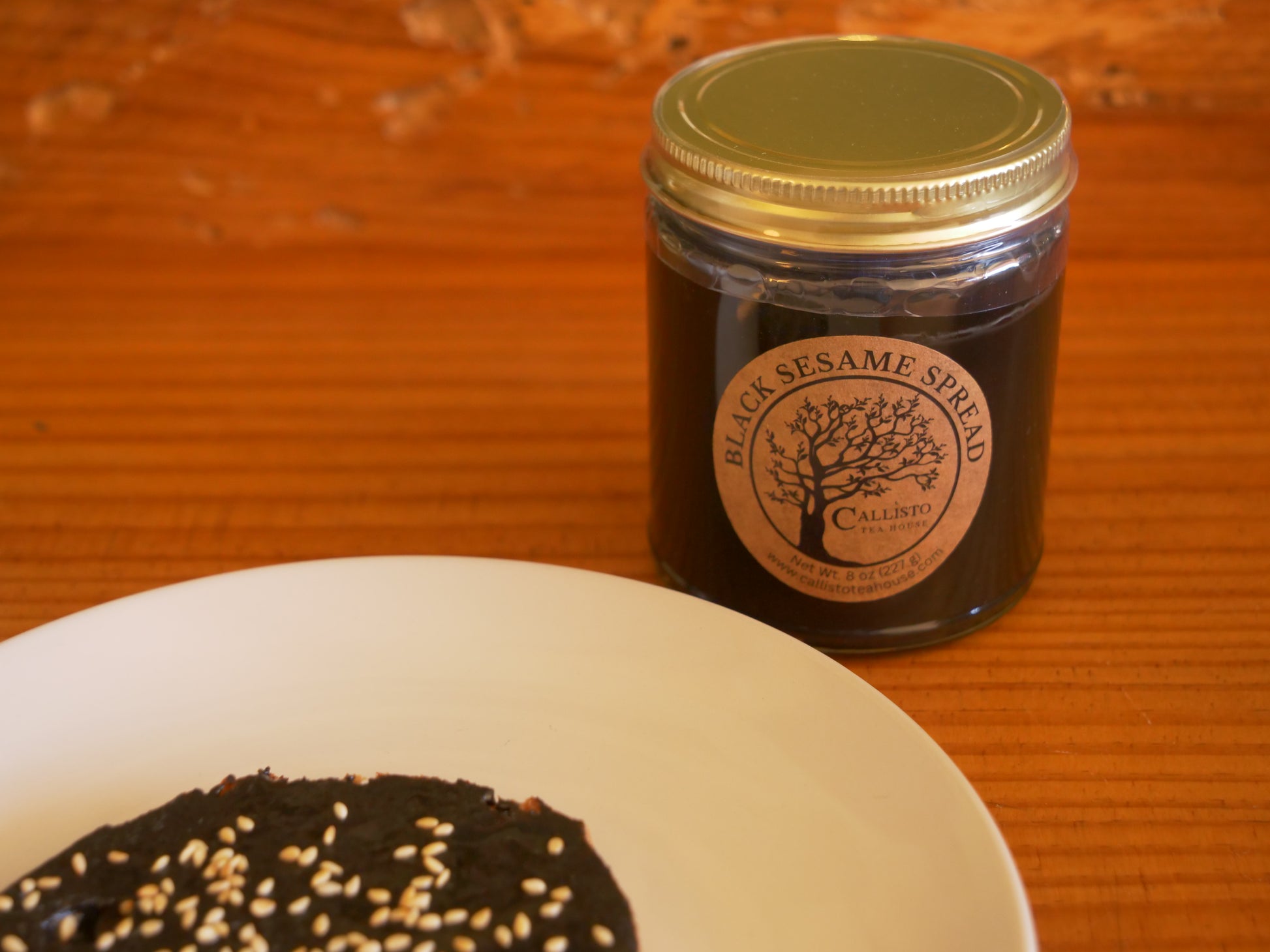 Jar of black sesame spread on a wooden surface with a spreadable product on a plate.