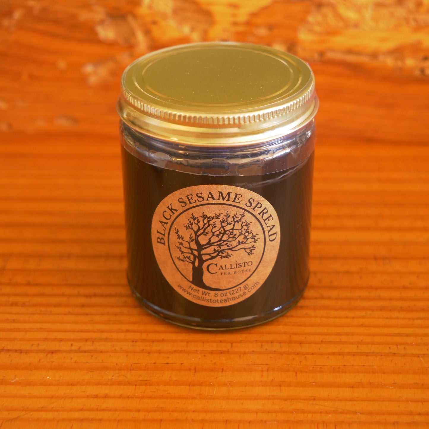 Jar of black sesame spread with a gold lid on a wooden surface
