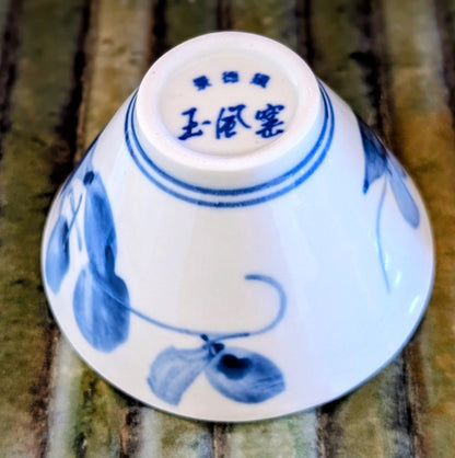 Bottom of a white porcelain tea cup with blue painted leaf design and Chinese characters on a wooden mat.