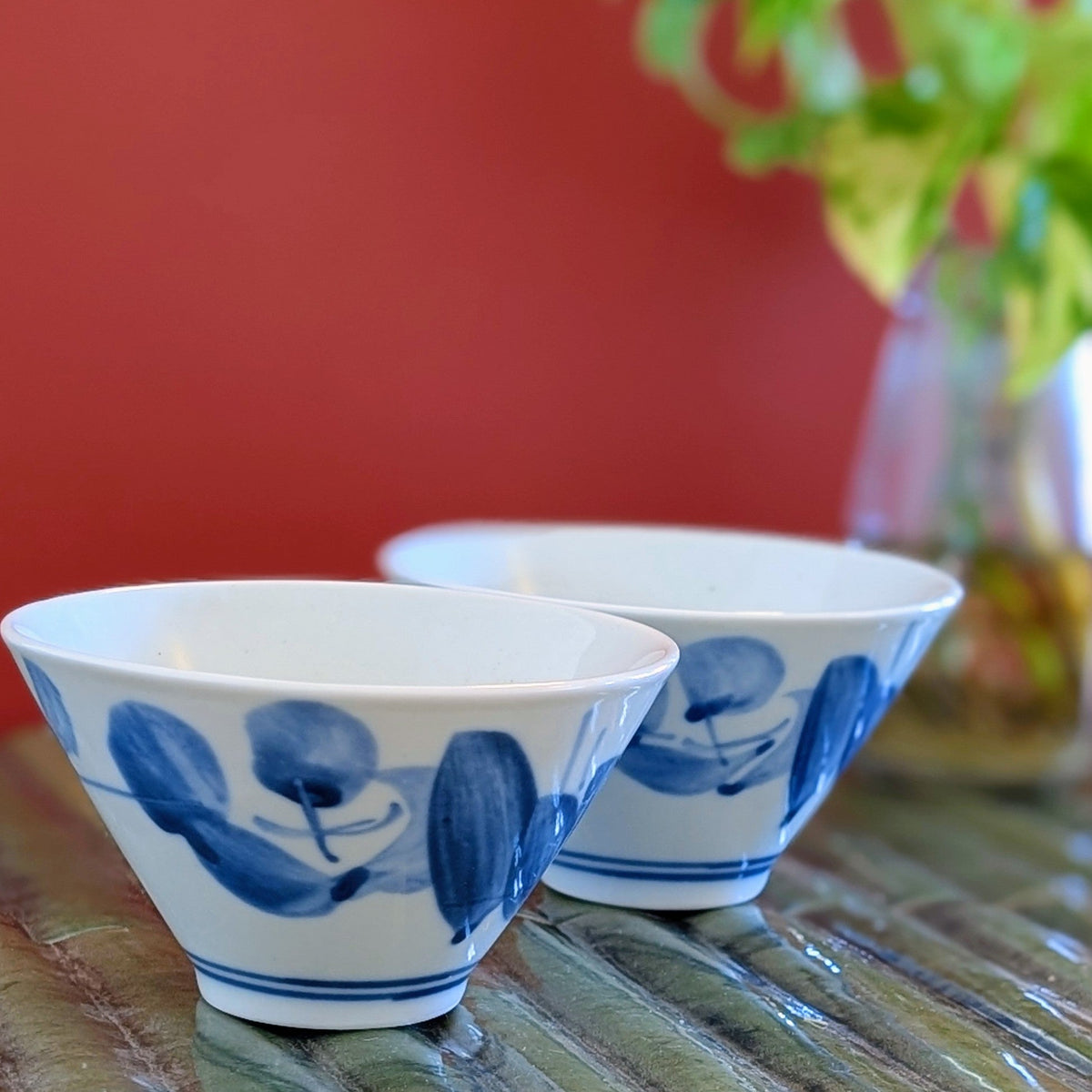 Two white porcelain tea cups painted with blue leaf design on a green mat against a terracotta background.