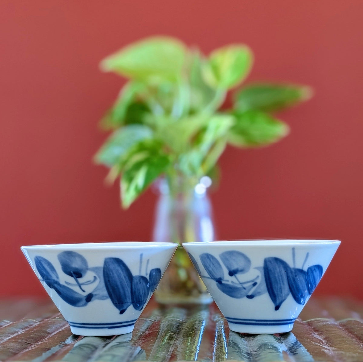 Two white porcelain tea cups painted with blue leaf design on a green mat against a terracotta background.