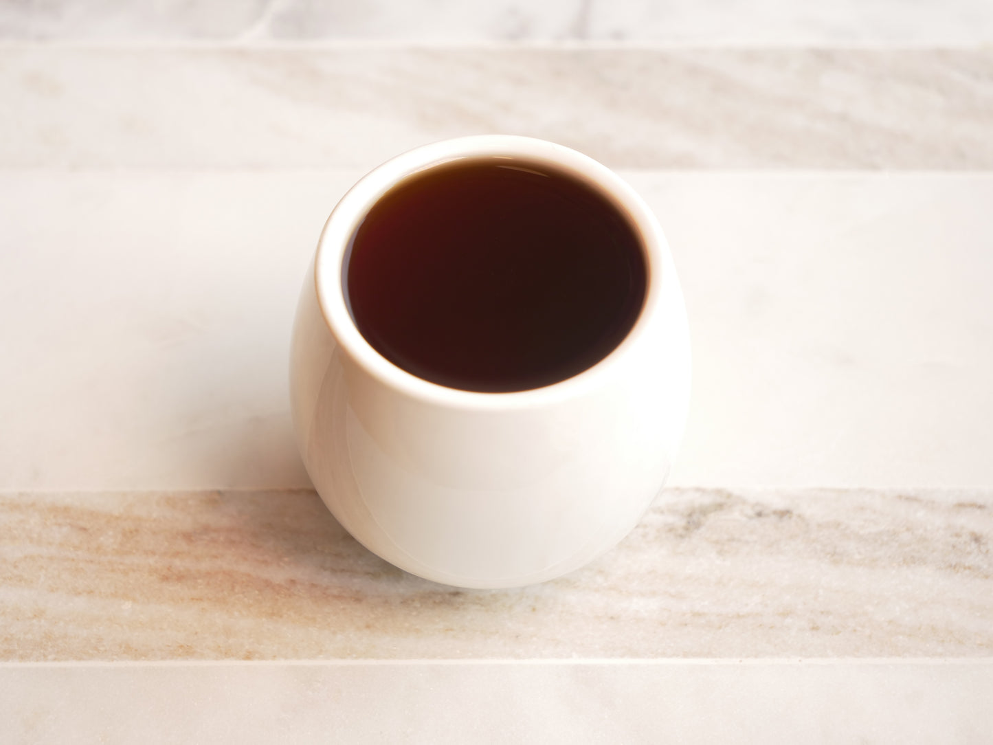 White ceramic cup filled with dark liquid on a marble surface