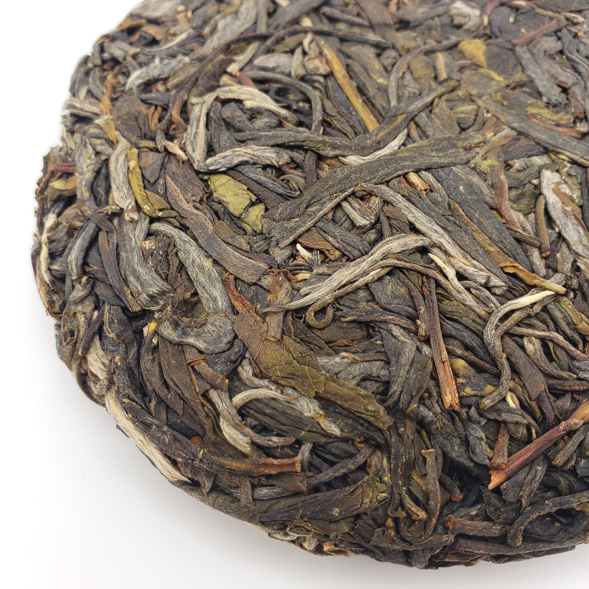 A close up of a compressed raw Puer premium tea cake, showing variety of color and leaf shape.