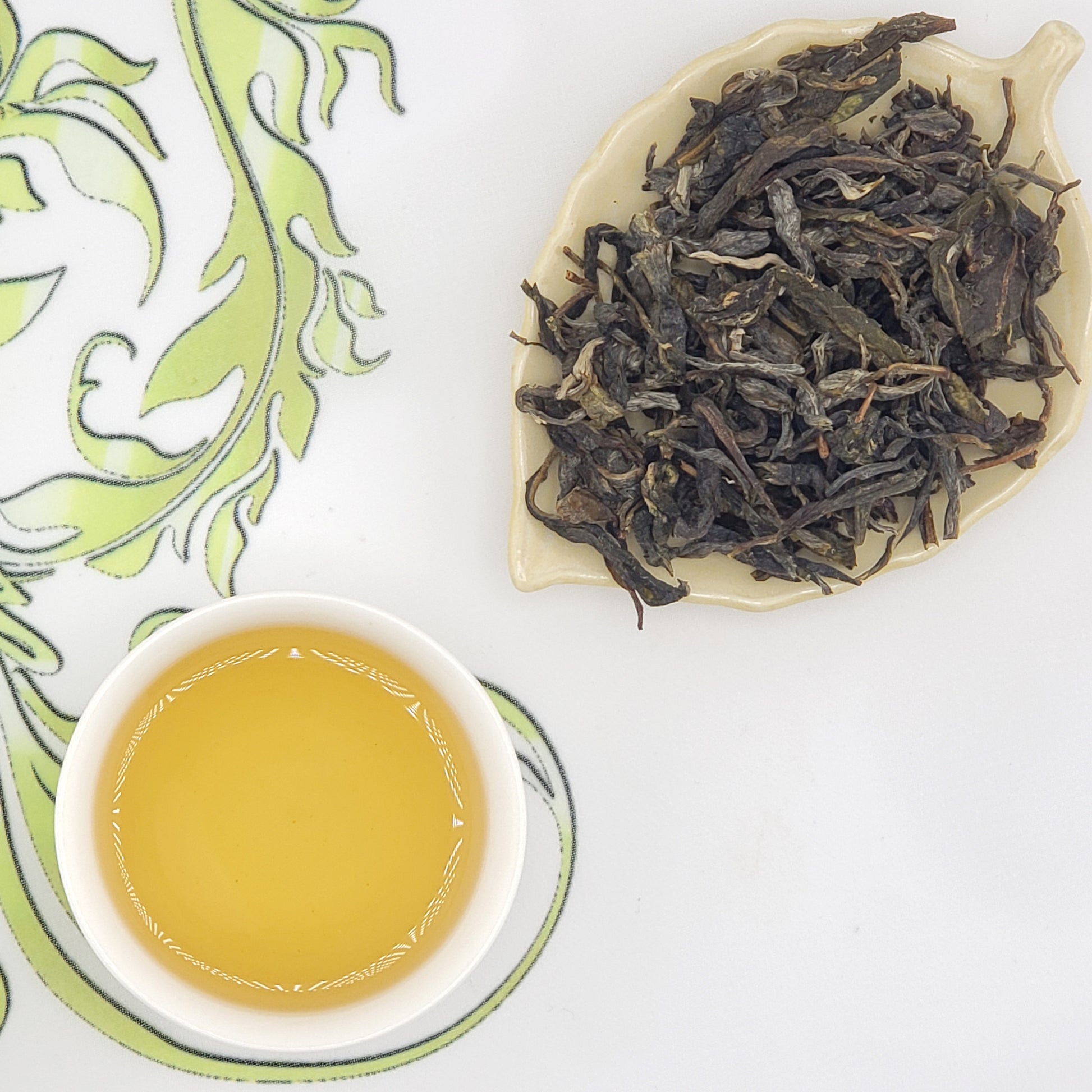 Specialty loose leaf Chinese tea next to a cup of golden hued tea.