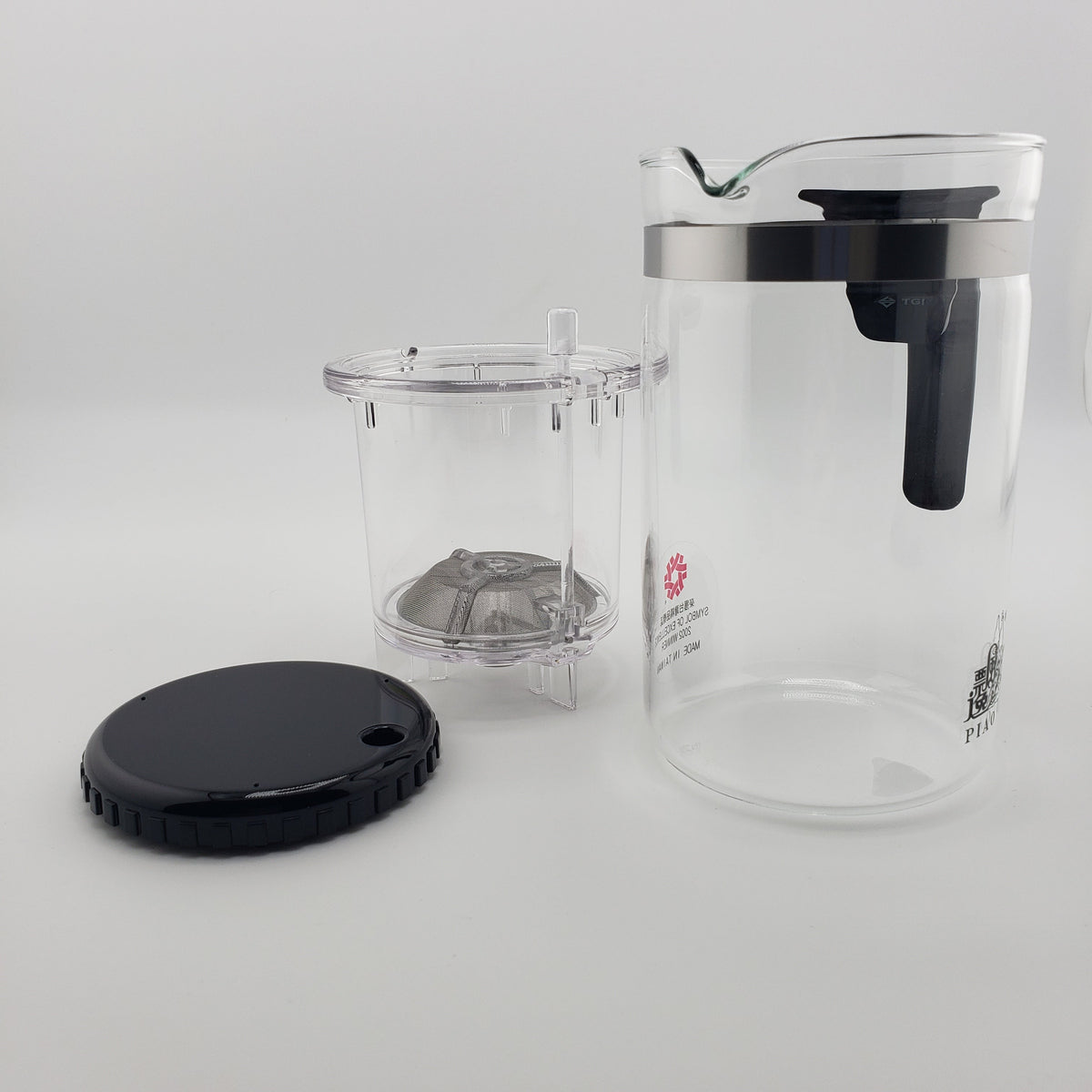 A clear glass teapot with a black lid and handle, shown with its clear infuser basket and black lid on a light gray background.