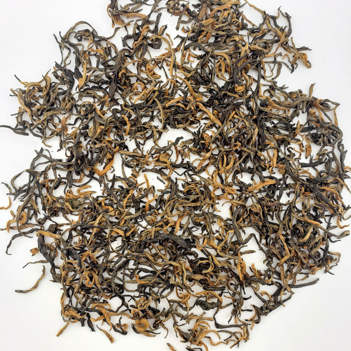 Dry black tea leaves with orange tips on a white background