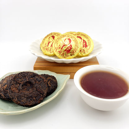 Tea leaves, a cup of tea, and gold wrapped tea coins on a white surface