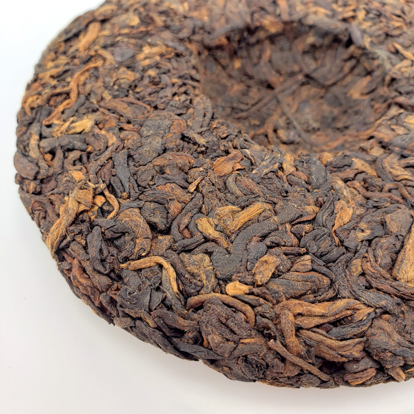 Close-up of a compressed shu Puerh tea cake with dark brown leaves on a white background