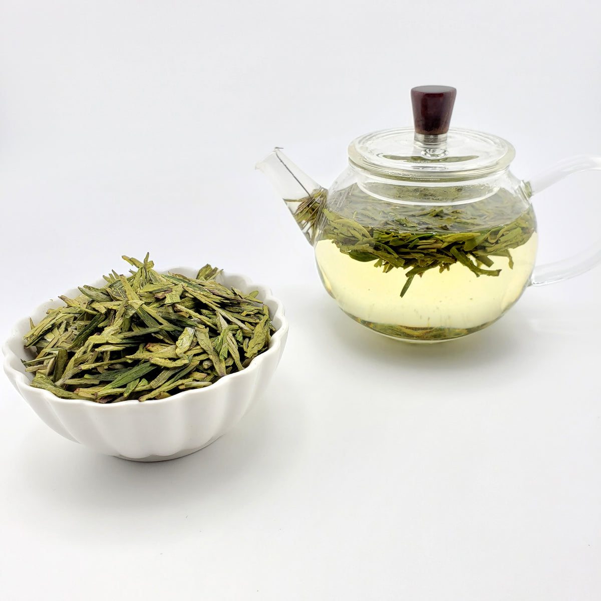 Glass teapot brewing green tea with loose tea leaves on a white background