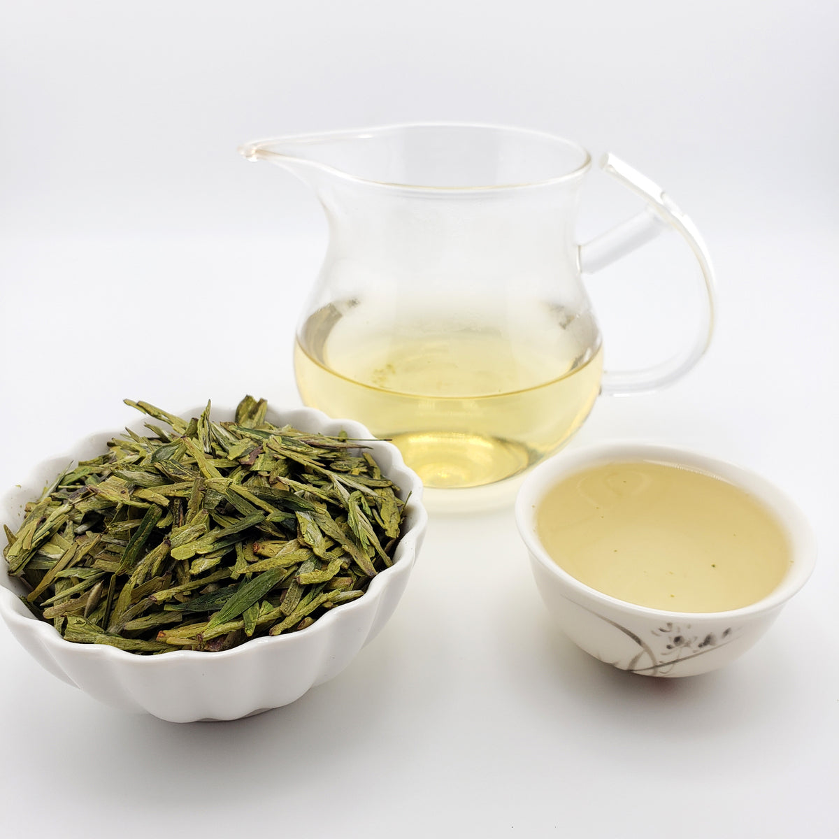 Tea leaves in a white bowl with a glass of brewed tea on a white background