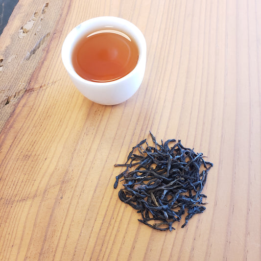 Dry black tea leaves and a cup of brewed tea on a wooden surface