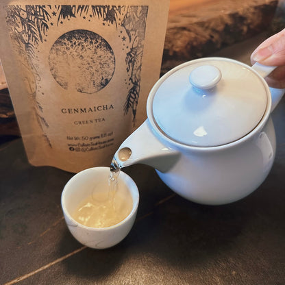 white teapot pouring tea into a cup in front of a package of Genmaicha tea