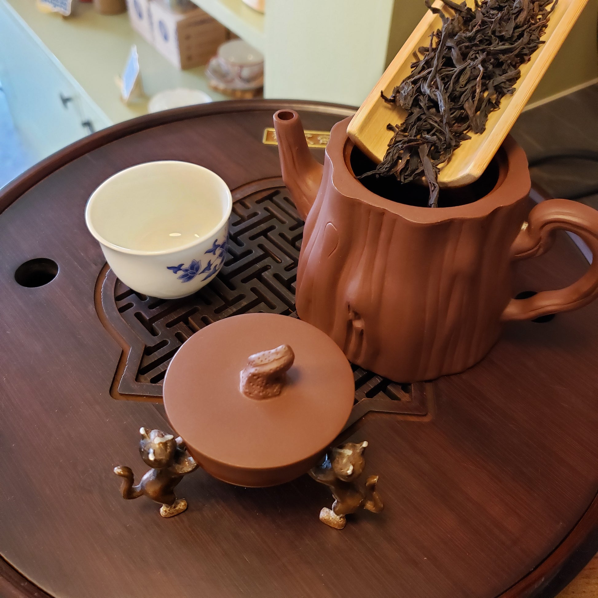 Tea set with a teapot, cup, and tea leaves on a wooden surface.