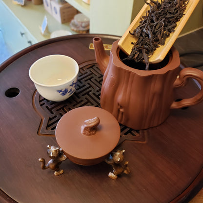 Tea set with a teapot, cup, and tea leaves on a wooden surface.