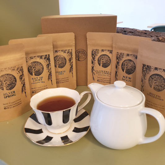 White teapot and black and white striped cup with tea, surrounded by packages of loose tea on a light green surface.