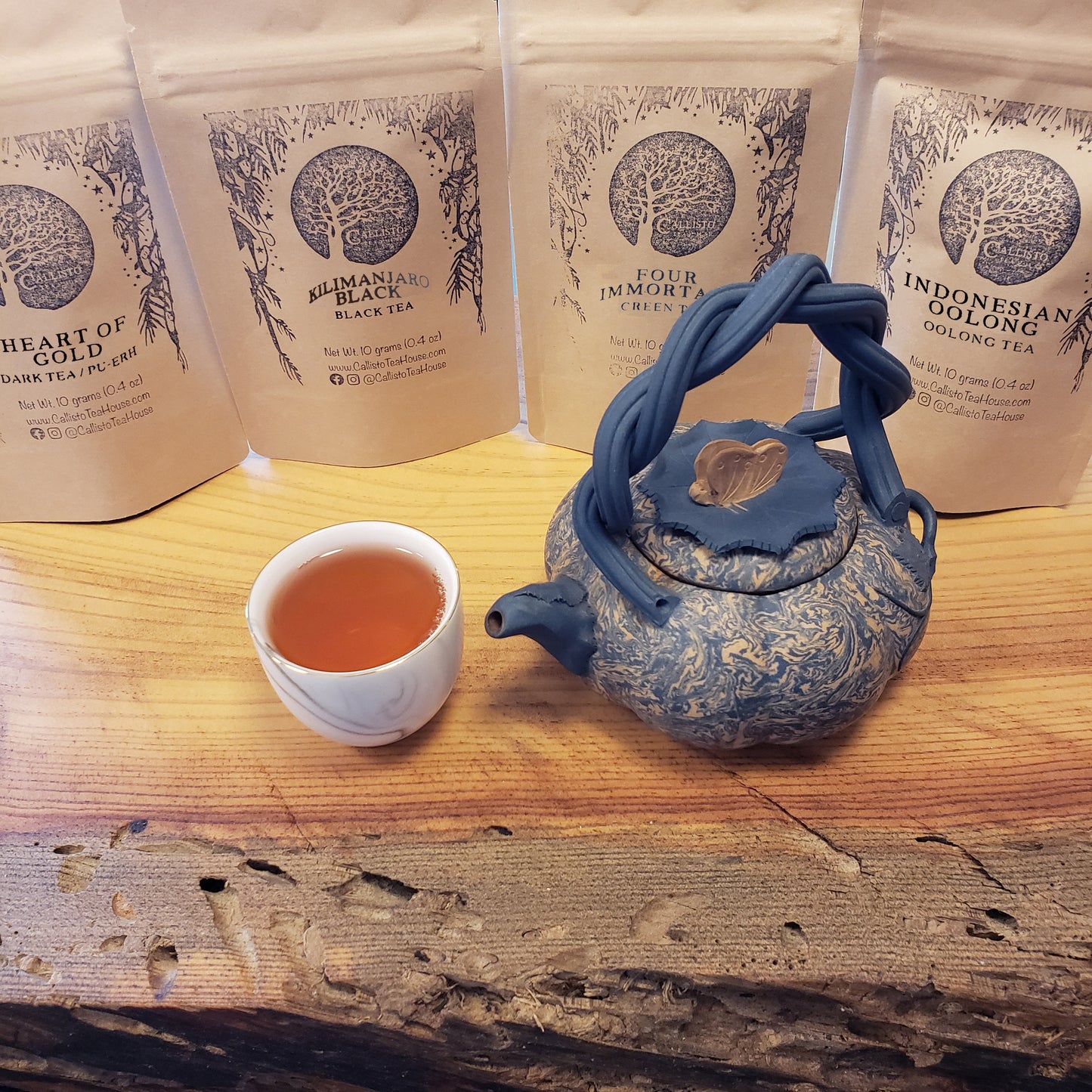 Blue teapot and cup on a wooden surface with packages of loose tea in the background