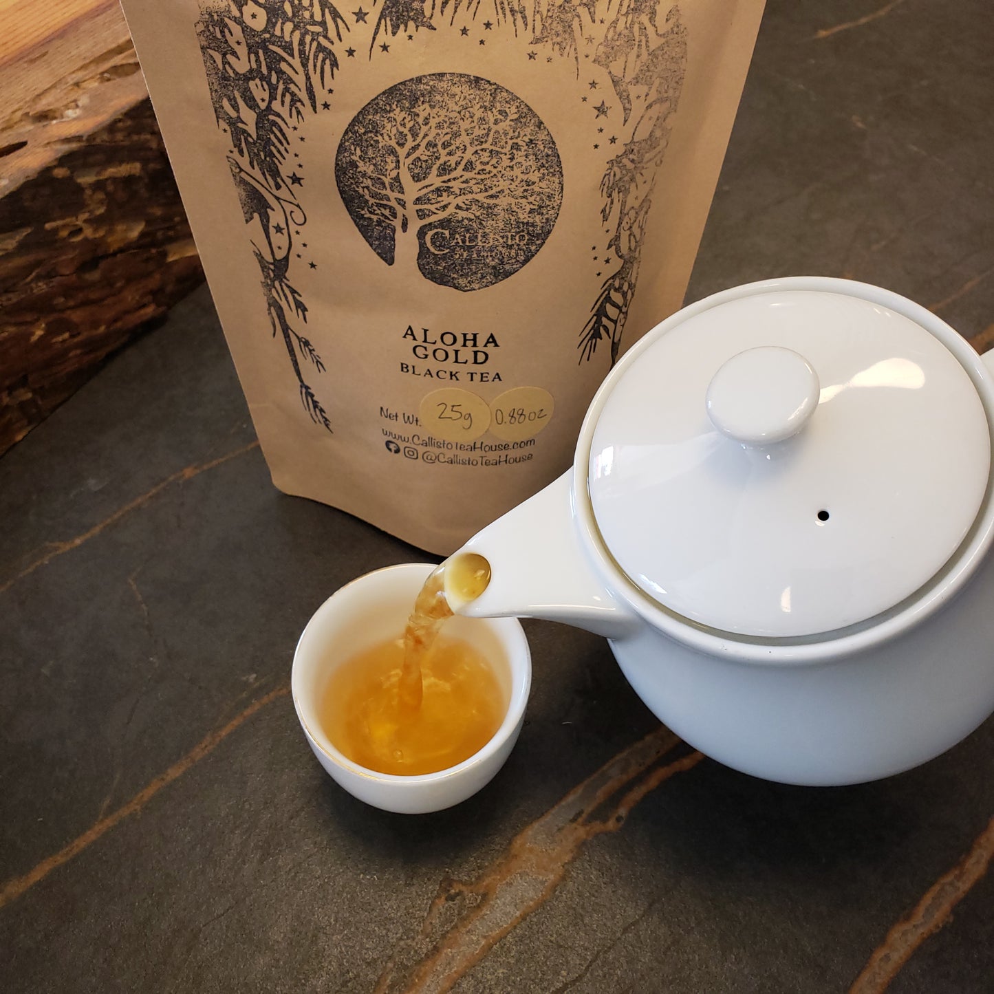 White teapot pouring tea into a white cup next to a tea bag on a stone surface