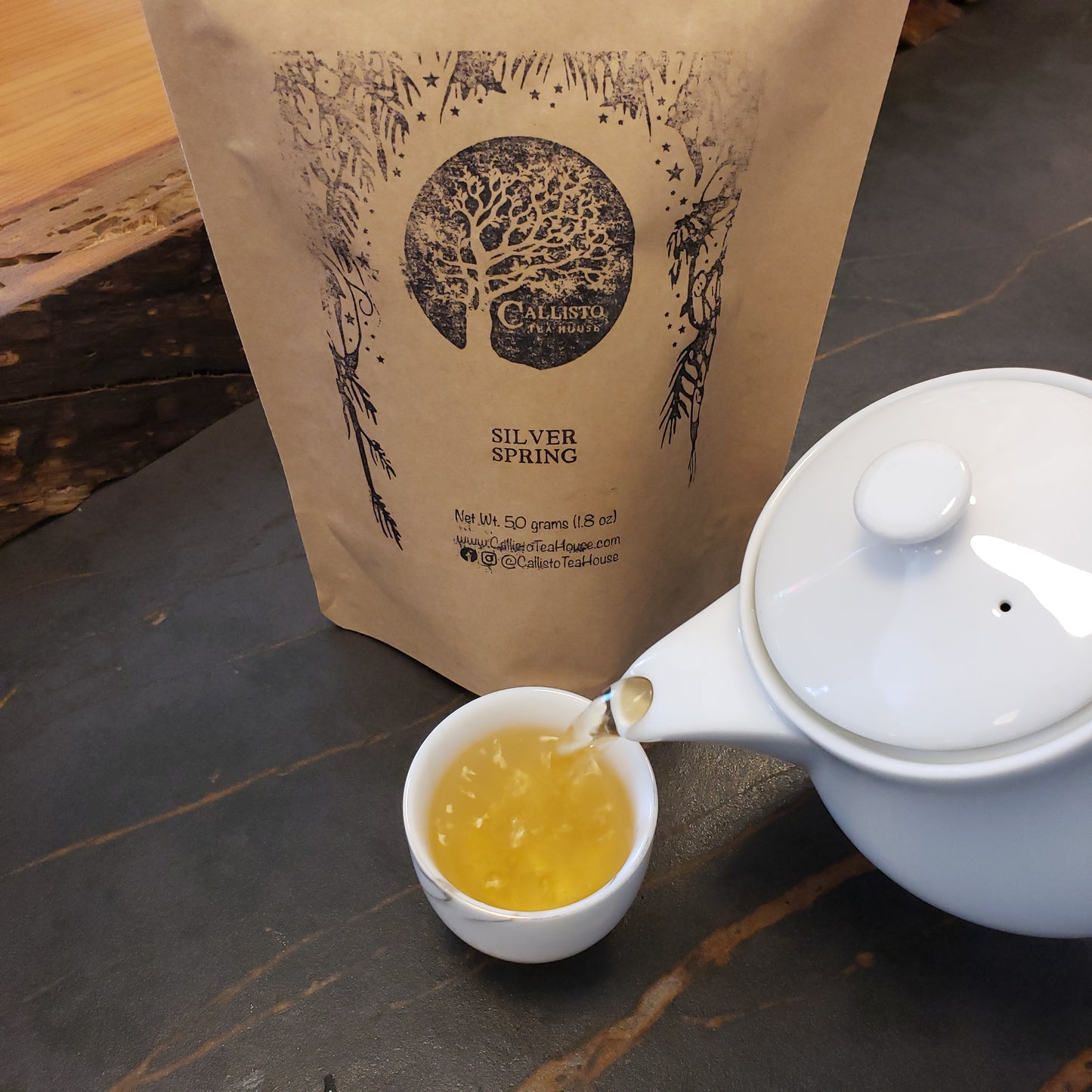 Tea being poured into a cup from a teapot on a wooden surface