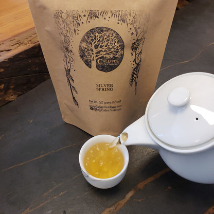 Tea being poured into a cup from a teapot on a wooden surface