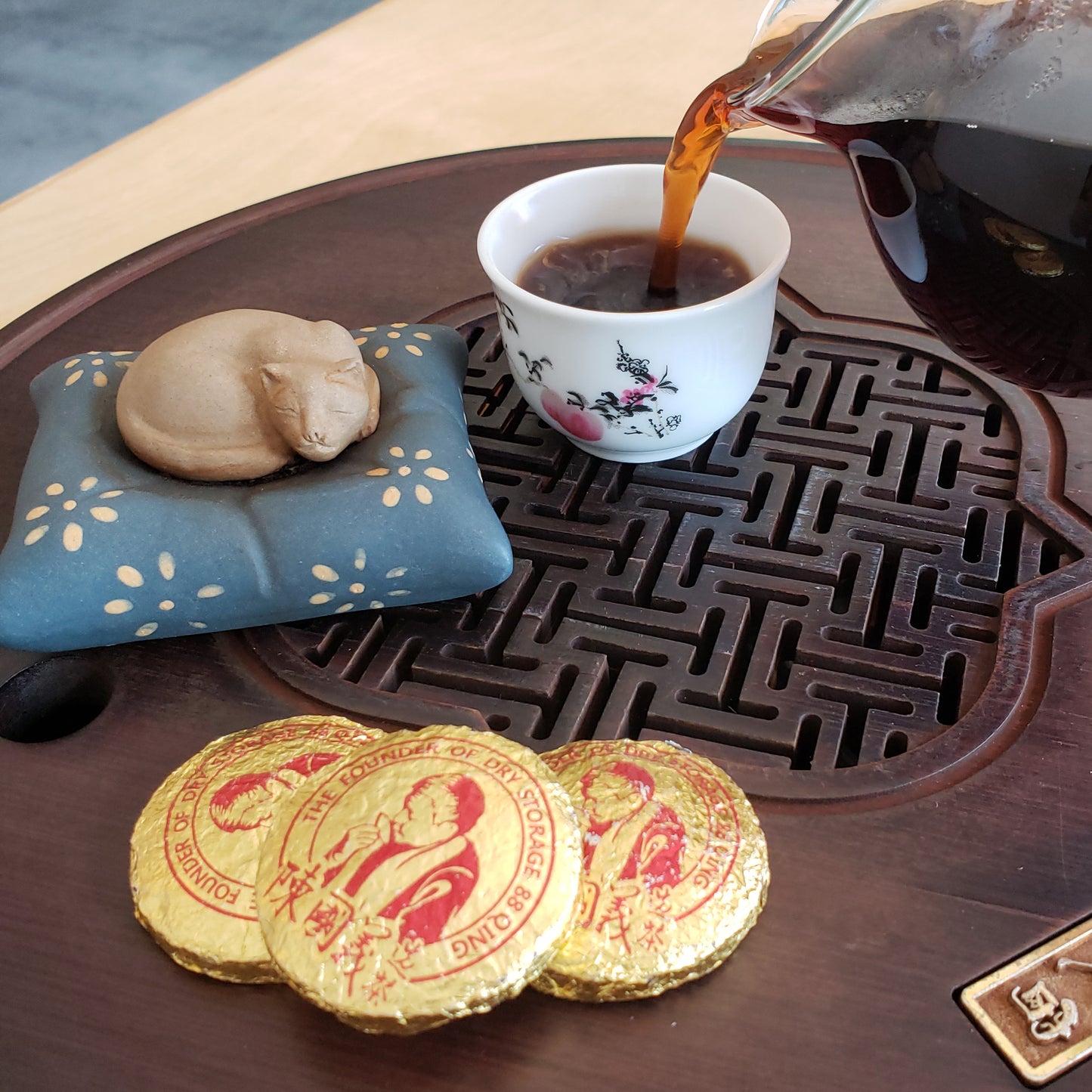 Tea being poured into a cup on a wooden tea tray with decorative elements.