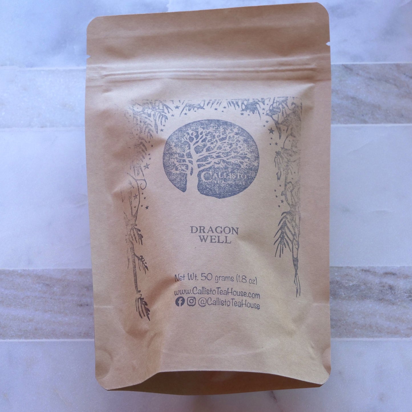Brown paper tea bag with 'Dragon Well' text and Callello Tea House branding on a marble surface.