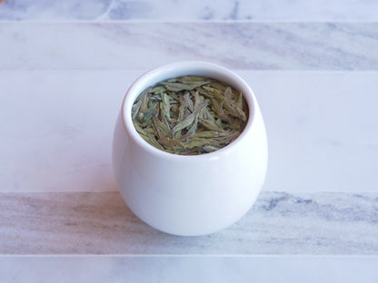 White ceramic container with green tea leaves on a marble surface