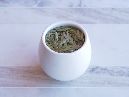 White ceramic container with green tea leaves on a marble surface