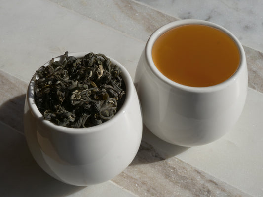 White bowl with dry tea leaves next to a cup of brewed tea on a marble surface