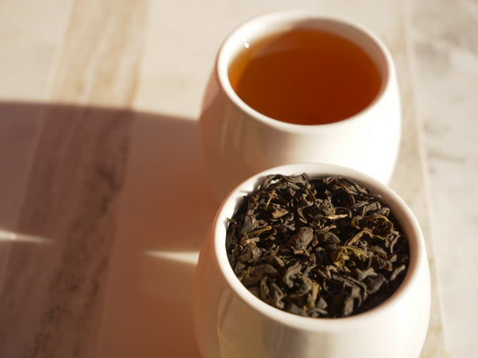 Two white bowls containing tea leaves and brewed tea on a wooden surface.