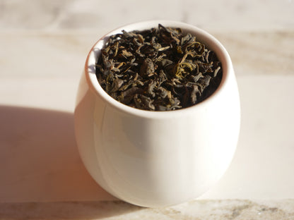 White ceramic cup filled with green tea leaves on a light background