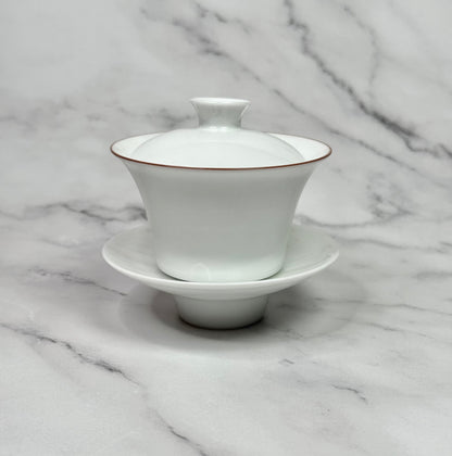 White porcelain gaiwan wih a red rim around the bowl.