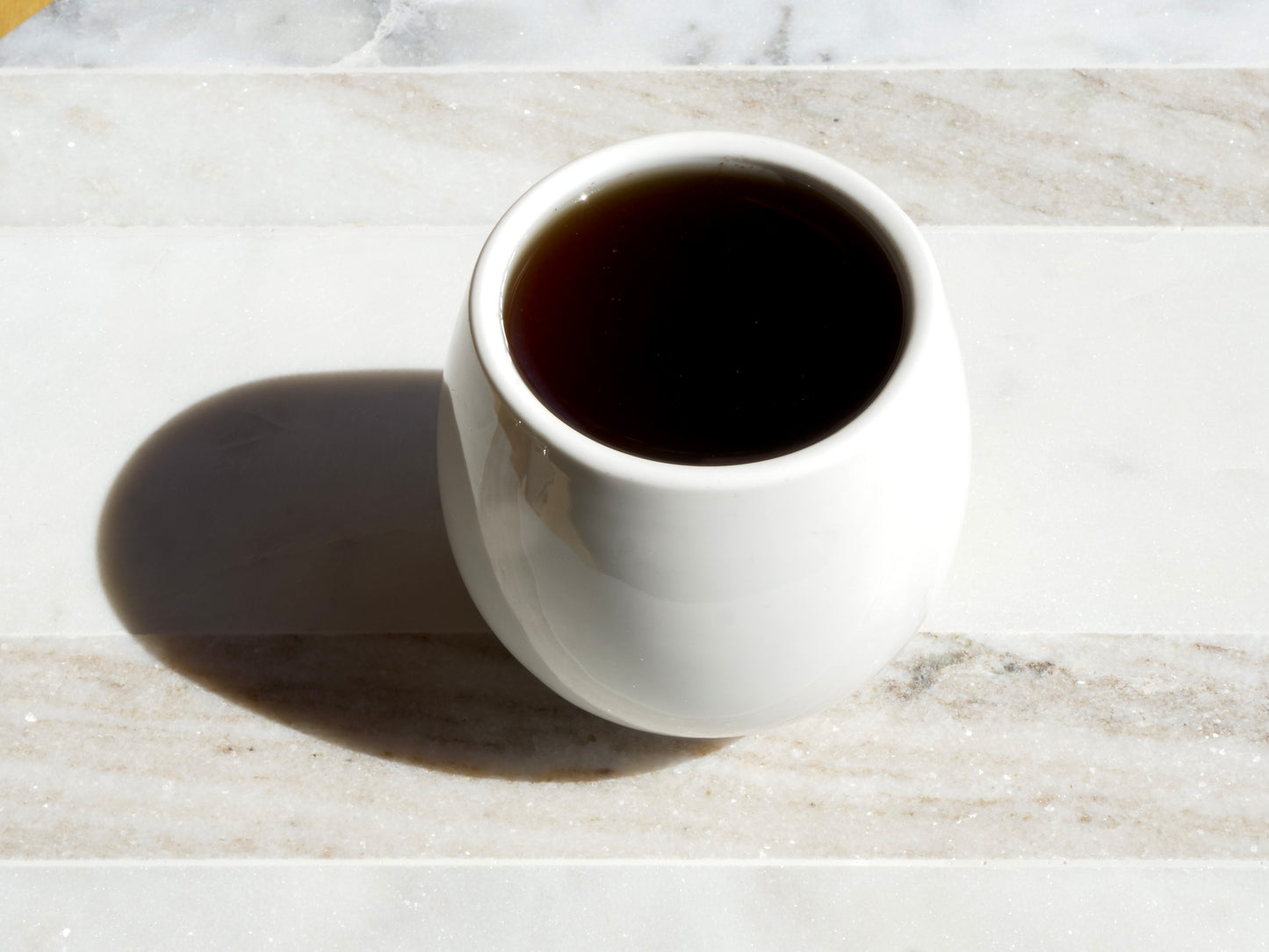 White mug filled with dark tea on a marble surface